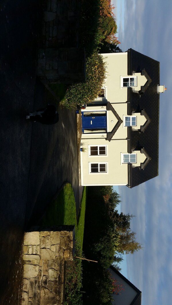 A two-story house with a blue door, a stone wall, and a lawn.