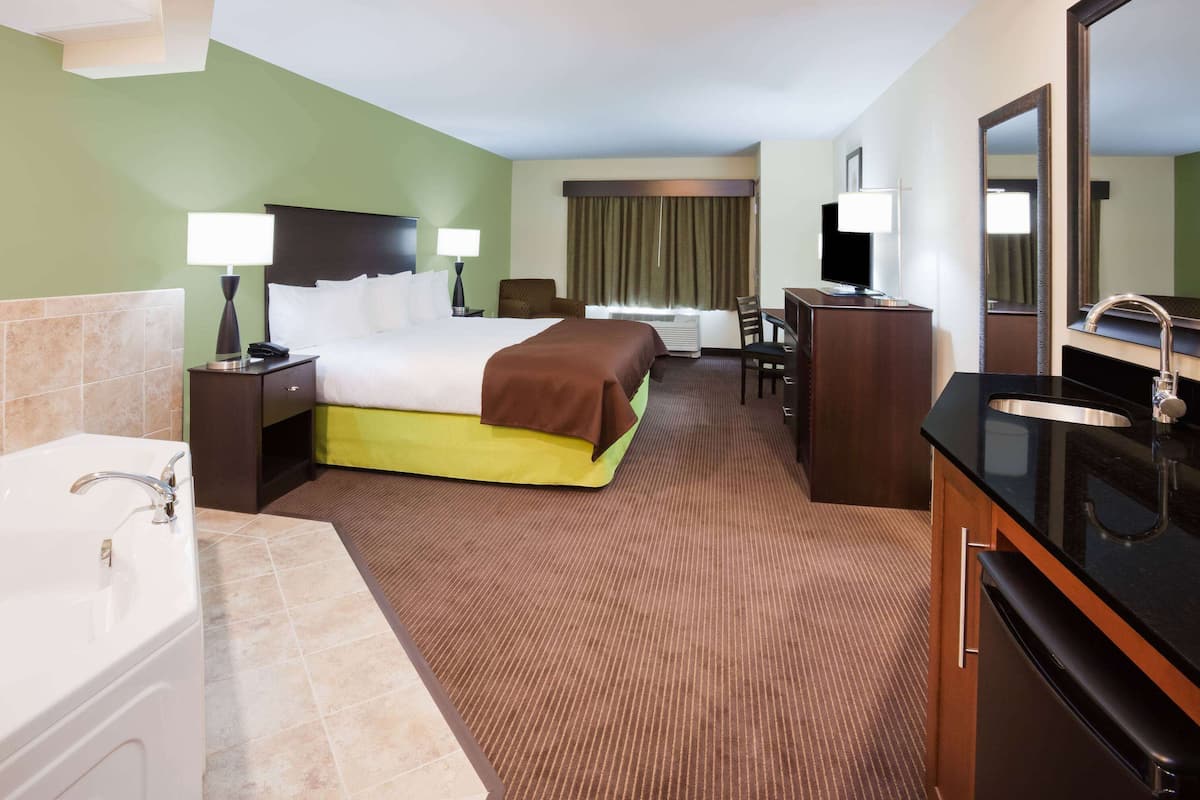 A hotel room with a bed, a desk, a chair, a TV, a bathroom with a sink and bathtub, and a mirror.