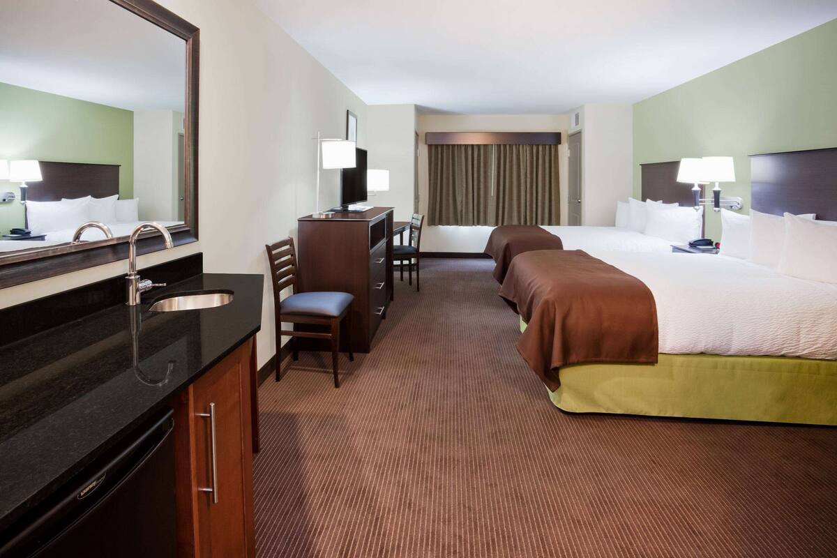 A hotel room with a large bed, a desk with a computer, a chair, a sink, and a mirror.