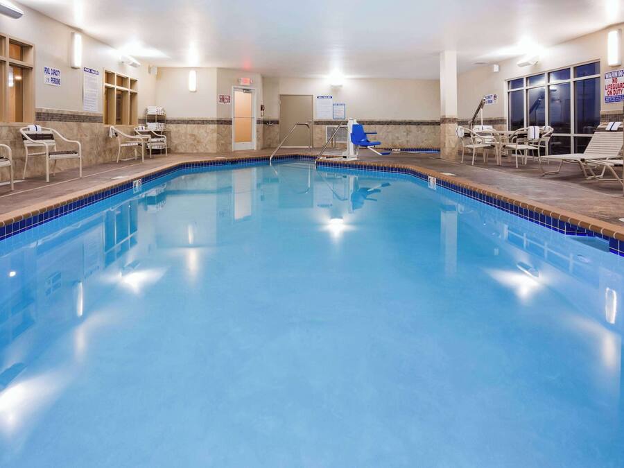 A large indoor swimming pool with clear water, surrounded by lounge chairs and a lifeguard chair.