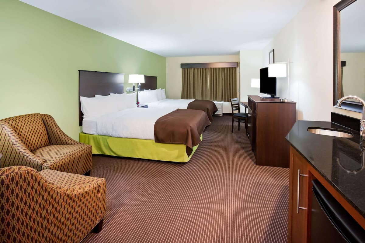 A hotel room with a bed, two armchairs, a desk, a TV, and a bathroom.