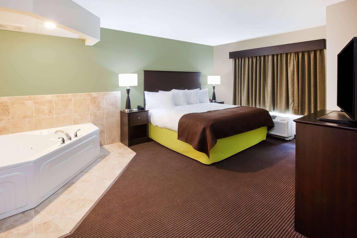 A hotel room with a large bed, a separate bathroom with a bathtub, a flat-screen TV, and a desk.