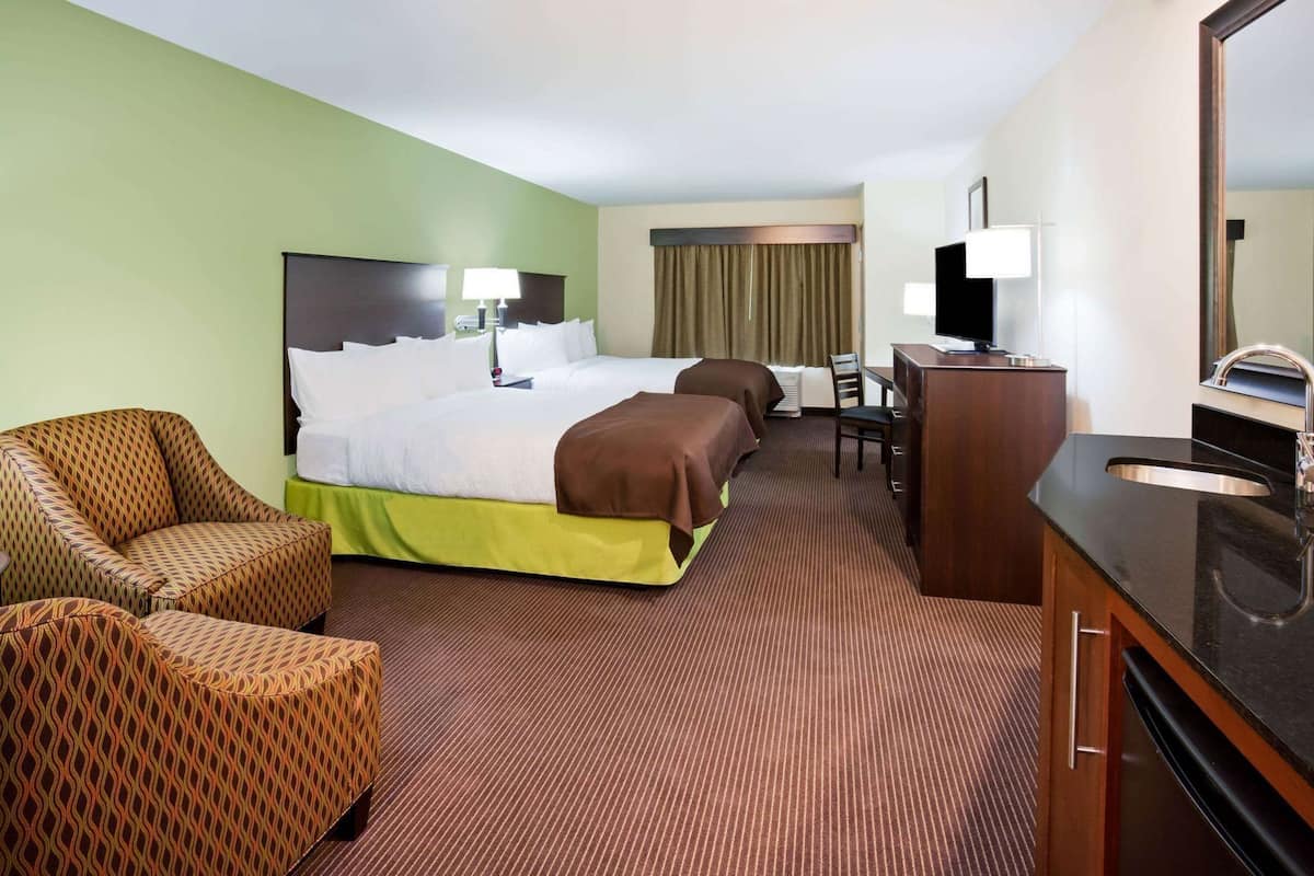 A hotel room with a bed, two armchairs, a desk, a TV, and a bathroom.