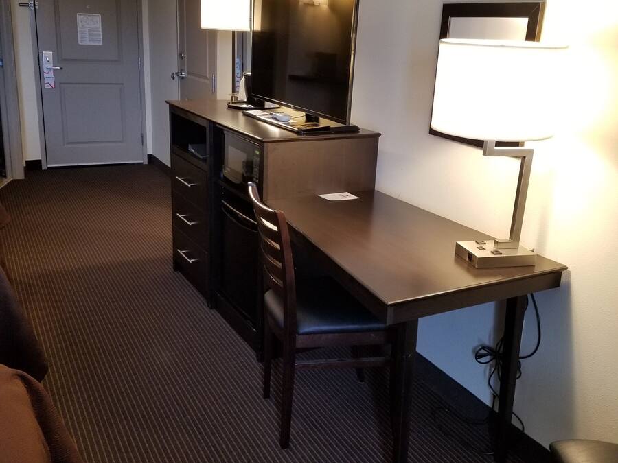 A hotel room with a desk, two chairs, a television, and a lamp.