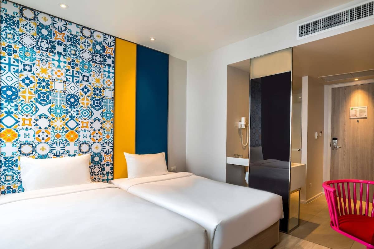 Habitación de hotel con pared estampada, una cama, una silla y un baño visible a través de un panel de vidrio.