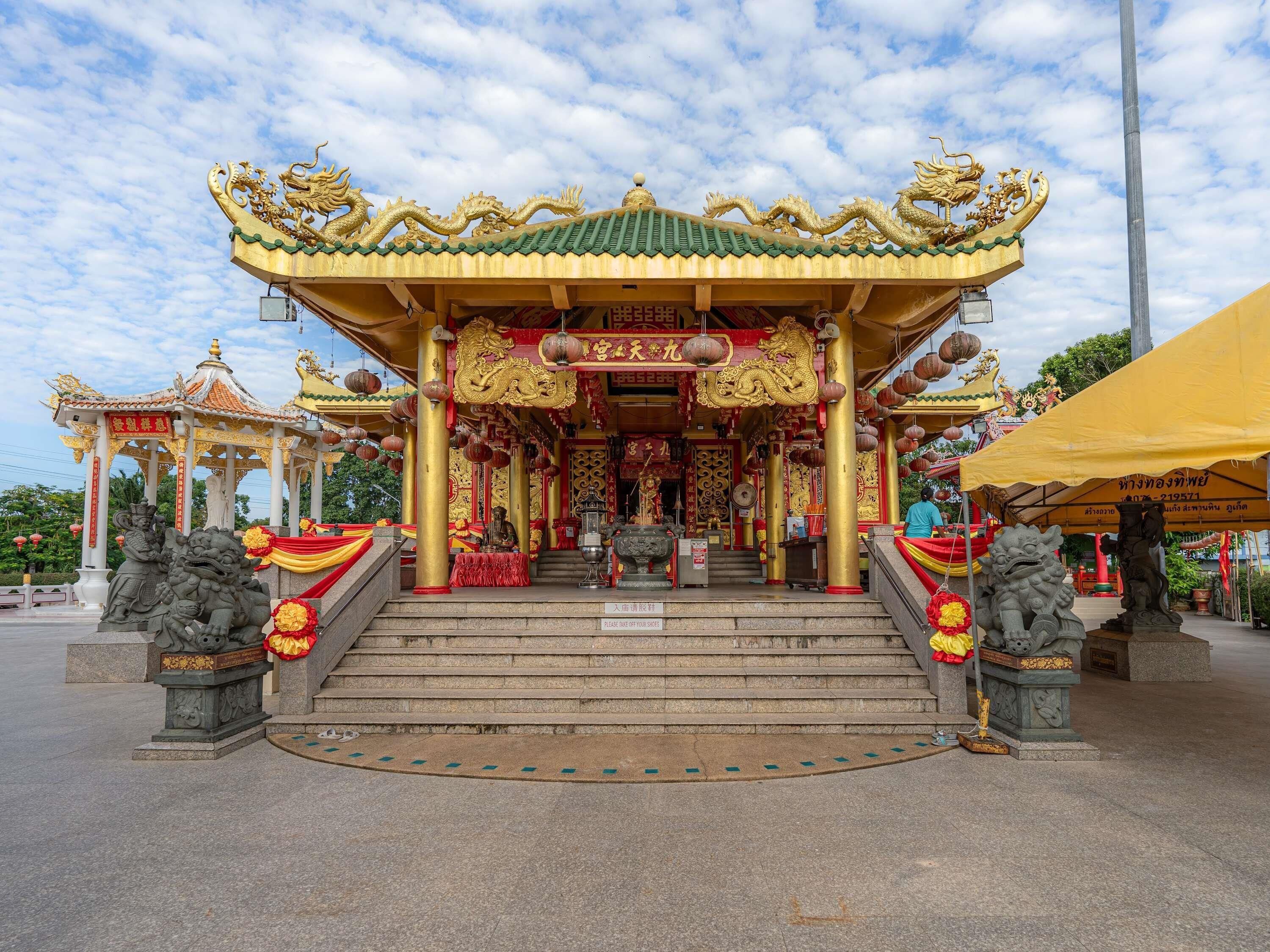 A traditional temple entrance with ornate golden decorations, a central statue, and a tiled roof.