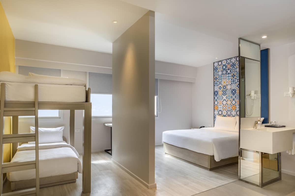 Una habitación de hotel con literas, una cama individual, un baño con espejo y una ventana.