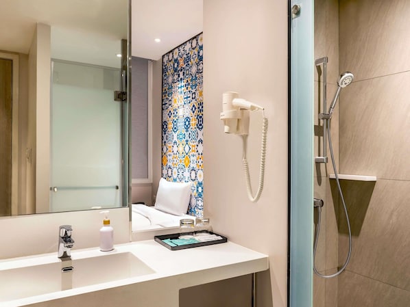 A bathroom with a mirror, a sink, a shower, and a patterned wall. - ibis Styles Phuket City Hotel (Phuket)