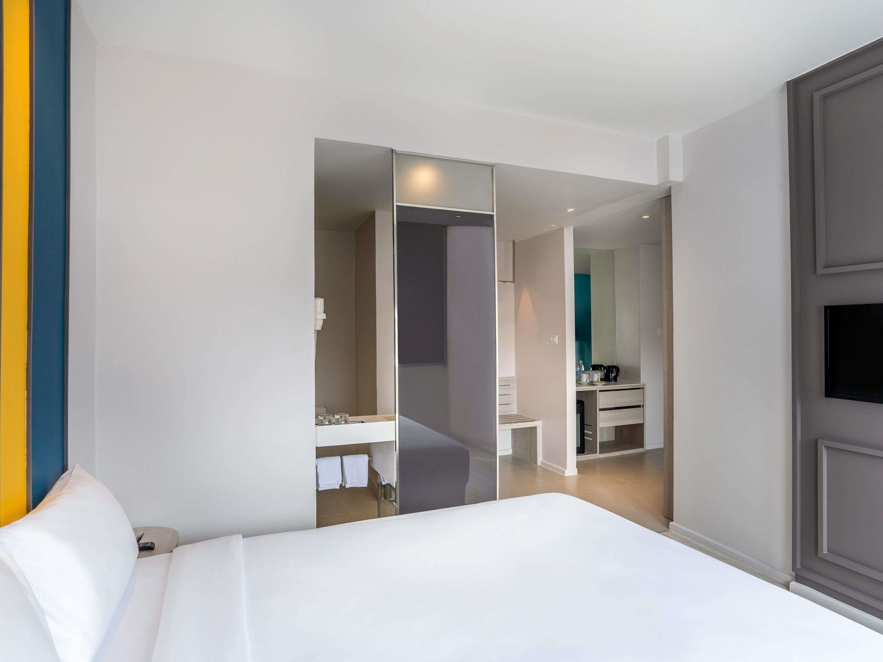 Quarto de hotel com cama, banheiro com espelho e televisão na parede.