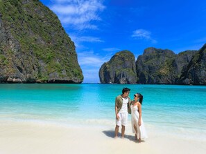 Een strand met helder turquoise water, wit zand en rotsachtige kliffen op de achtergrond.
