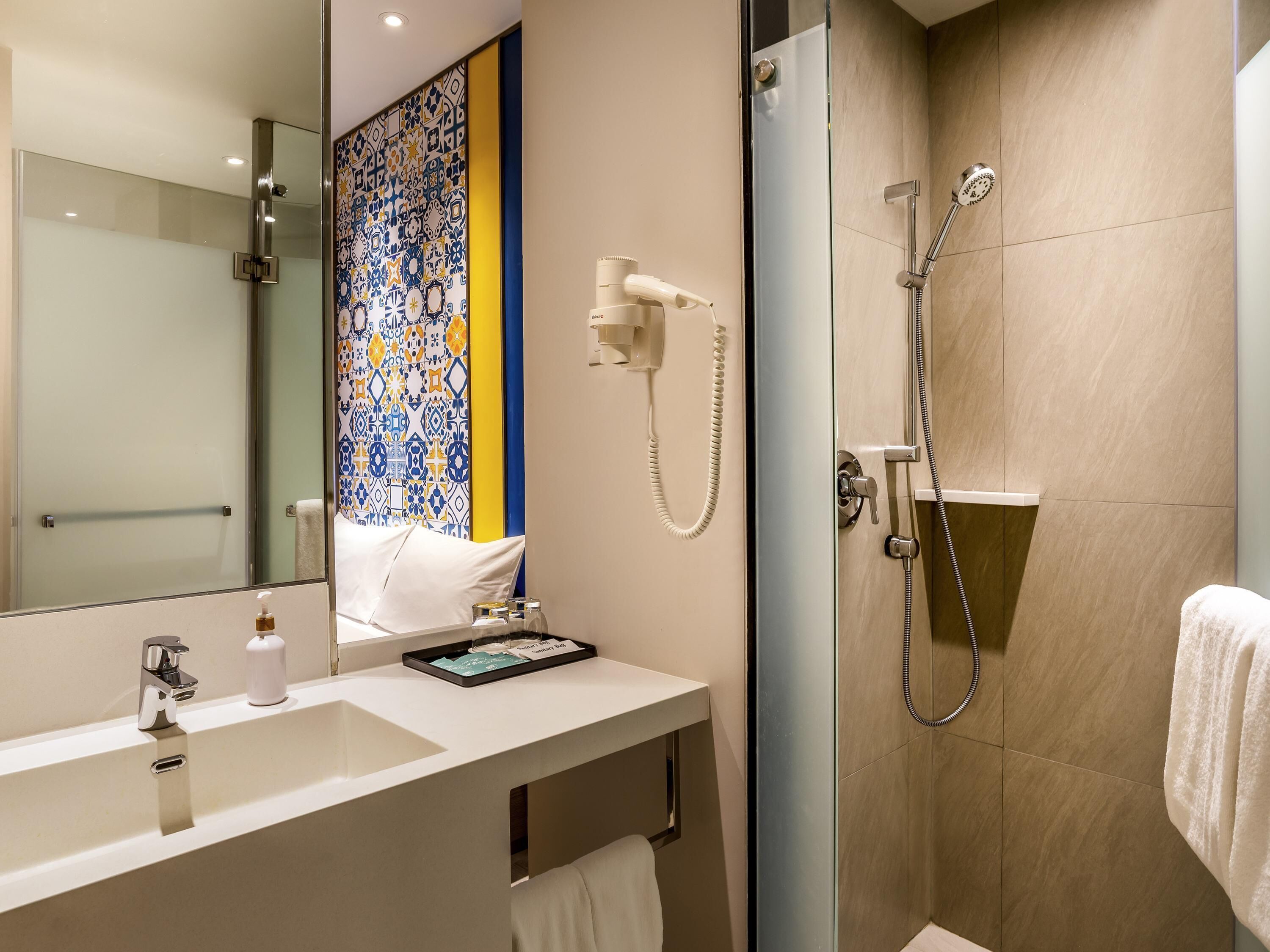 A modern bathroom with a glass shower enclosure, a white sink with a mirror, and a decorative tile wall.