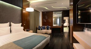 Quarto de hotel moderno com cama grande, área de estar, penteadeira e televisão.