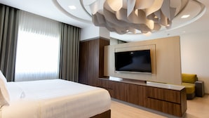 A modern hotel room with a large bed, a flat-screen TV mounted on a wooden console, a sofa, and a unique ceiling light fixture. - HS HOTSSON Hotel Irapuato (Irapuato)