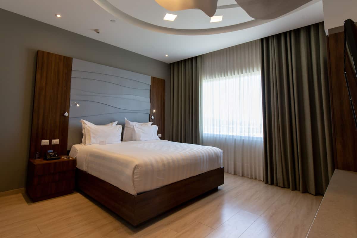 Ein modernes Hotelzimmer mit einem großen Bett, einem Holzkopfende und einem Nachttisch mit Telefon und Ladegerät.
