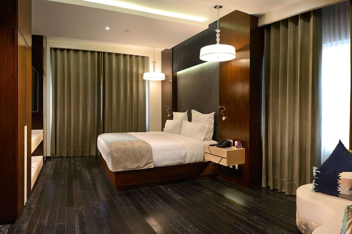 Ein modernes Hotelzimmer mit einem großen Bett, Holzboden, einem Nachttisch, einer Lampe und einem Sofa mit Kissen.