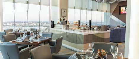Een moderne hotellobby met een bar, een eetruimte en uitzicht op de stad.