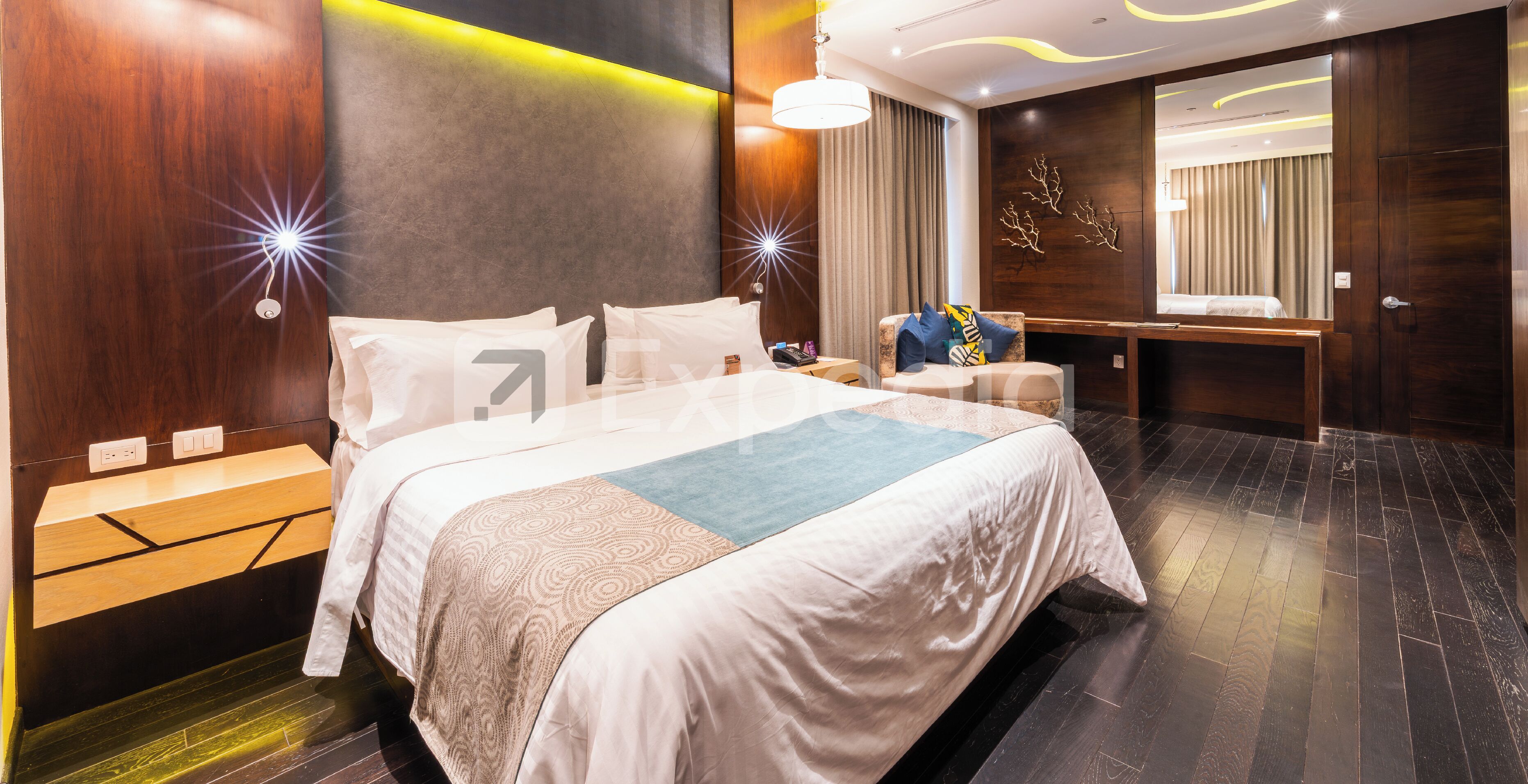 Una habitación de hotel moderna con una cama grande, mesitas de noche, un escritorio y un espejo.