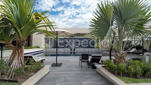 A hotel entrance with a pool area, lounge chairs, and palm trees. - HS HOTSSON Hotel Irapuato (Irapuato)