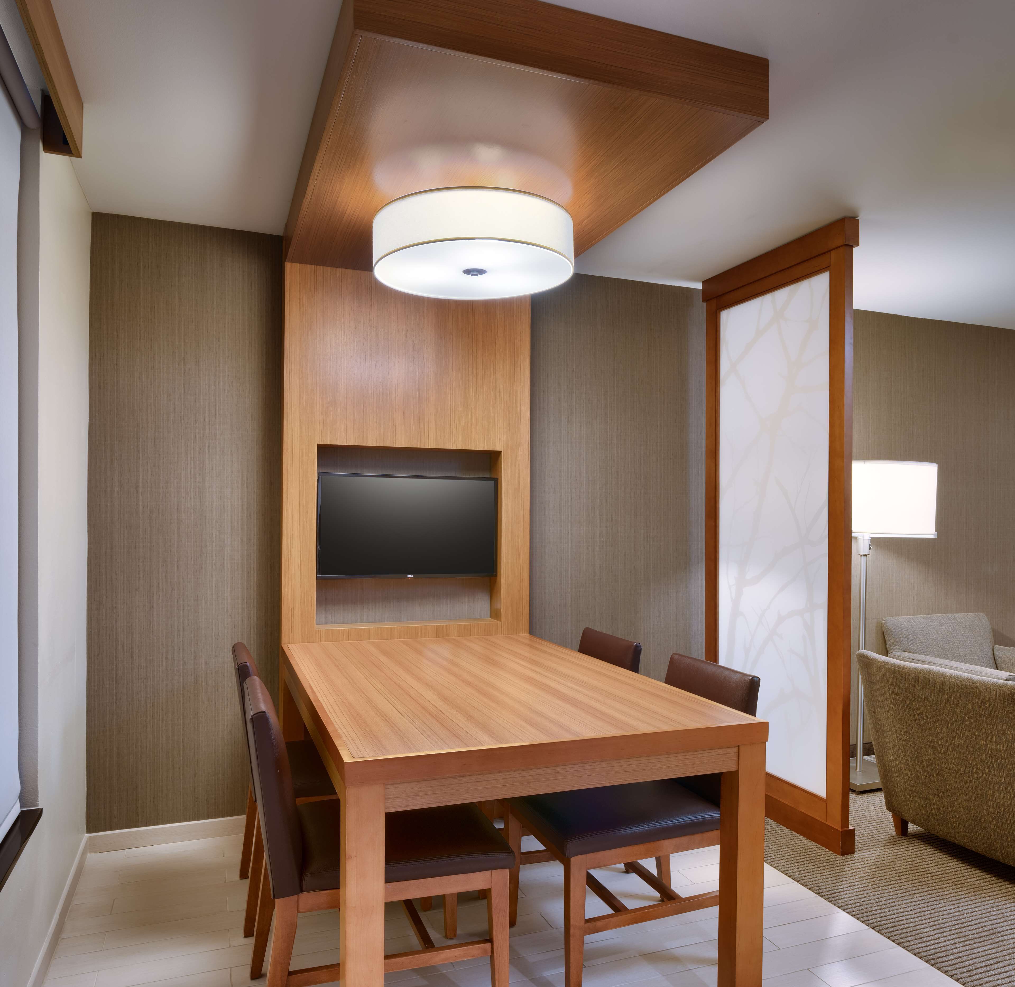 Una habitación de hotel moderna con una mesa de comedor de madera, seis sillas, un televisor de pantalla plana en la pared y un sofá.