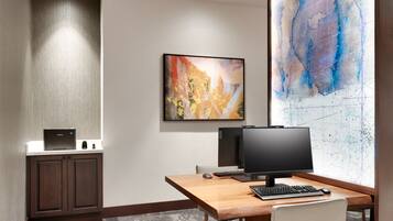 A hotel room with a desk, computer, and artwork on the wall.