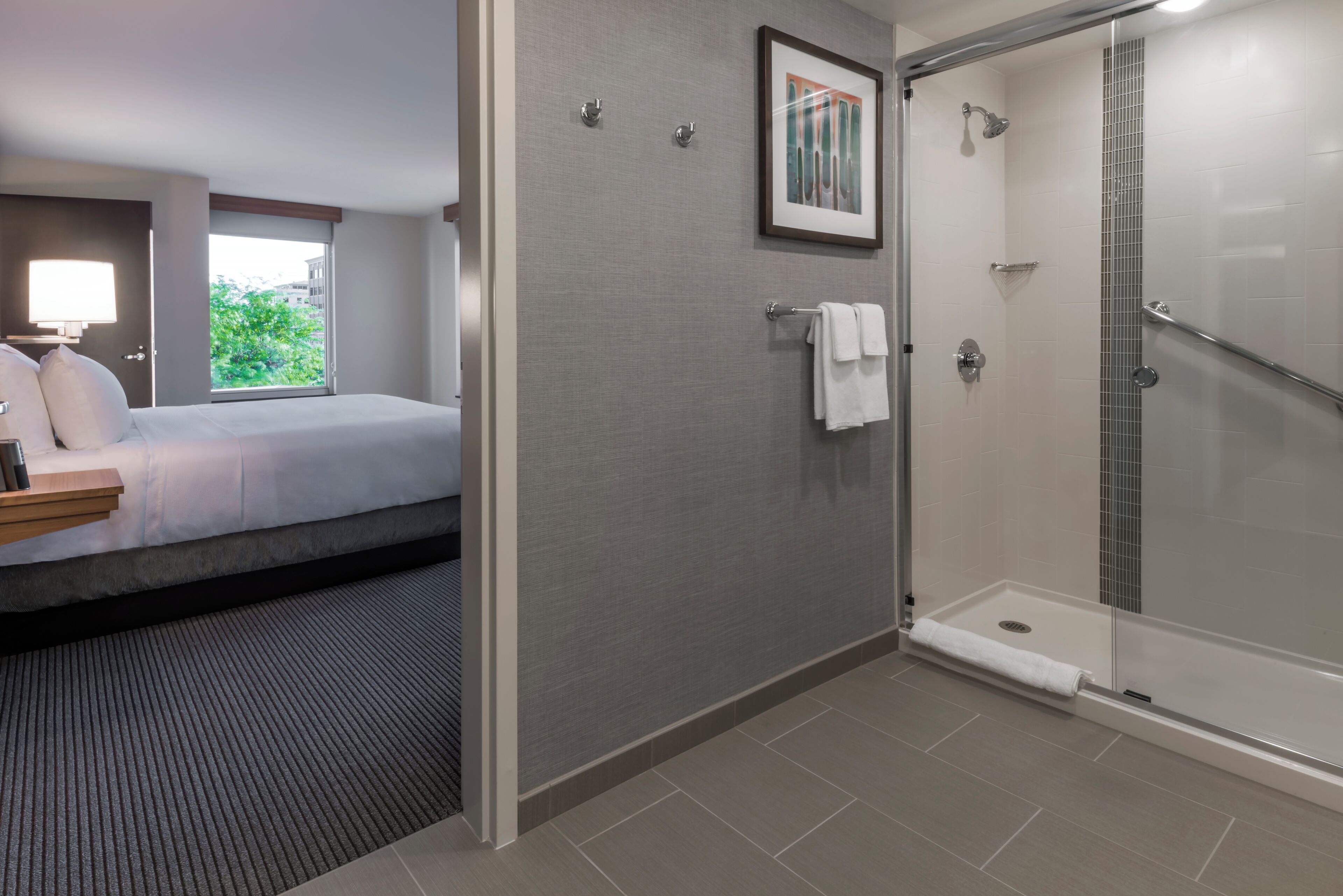 A hotel room with a bed, a shower, and a window with a view of greenery.