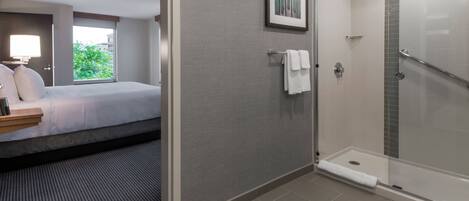 A hotel room with a bed, a shower, and a window with a view of greenery.