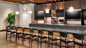 A modern bar area with a long counter, multiple bar stools, and a television screen. - Hyatt Place Boise/Downtown (Boise)