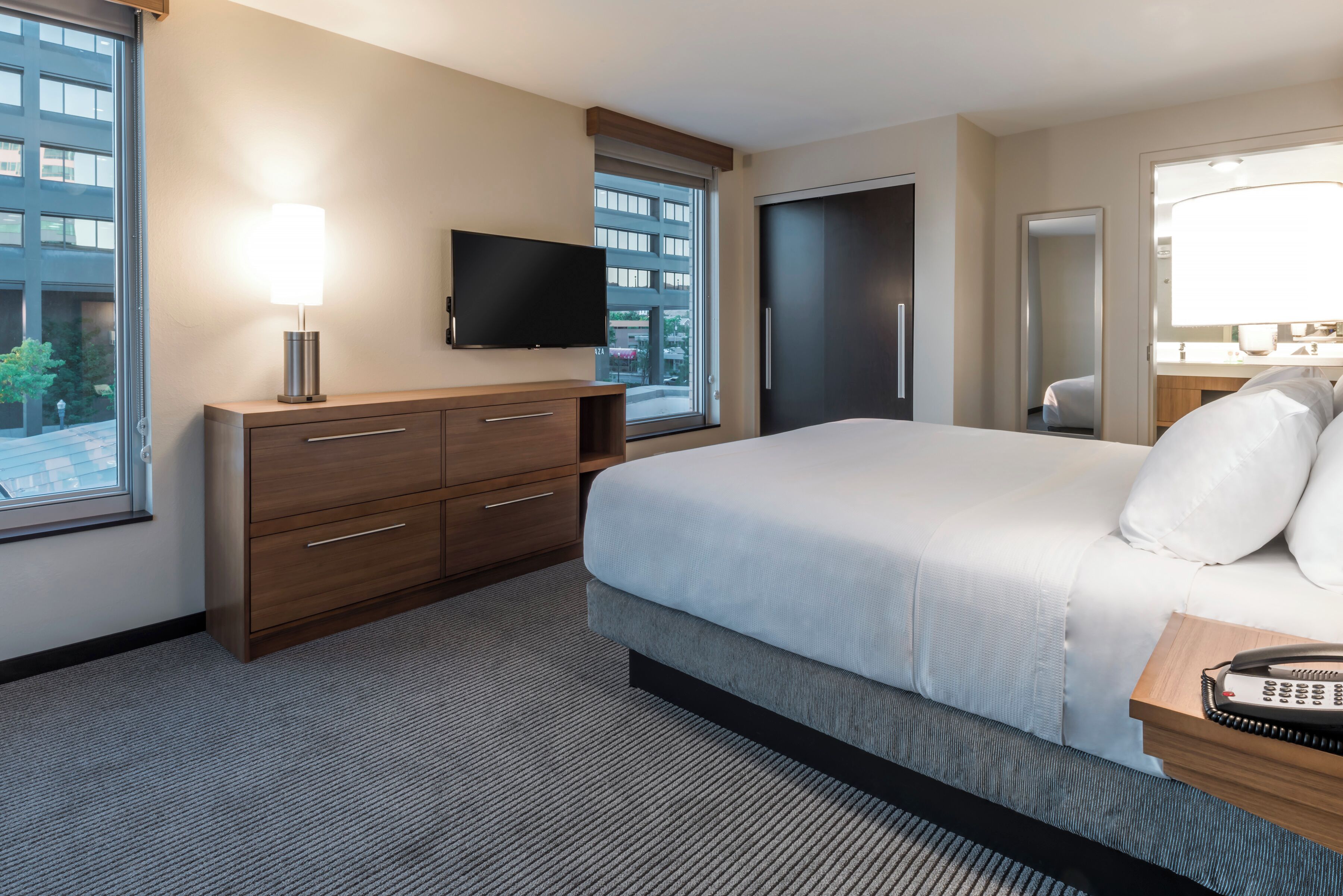 Une chambre d’hôtel avec un lit, une télévision, un bureau avec une lampe et une fenêtre donnant sur des immeubles.