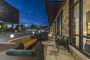 An outdoor seating area with wicker furniture and a yellow sofa, adjacent to a building with large windows and a brick facade. - Hyatt Place Boise/Downtown (Boise)