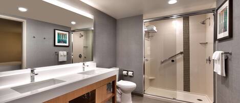 A modern bathroom with a large mirror, dual sinks, a toilet, and a glass-enclosed shower.