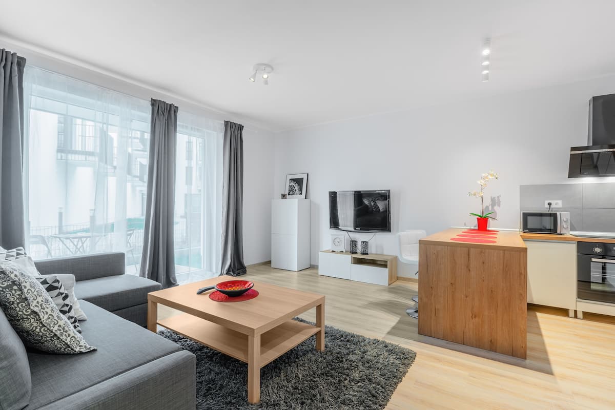 Un salon moderne comprenant un canapé, une table basse, un téléviseur et un coin cuisine avec un four à micro-ondes et un évier.