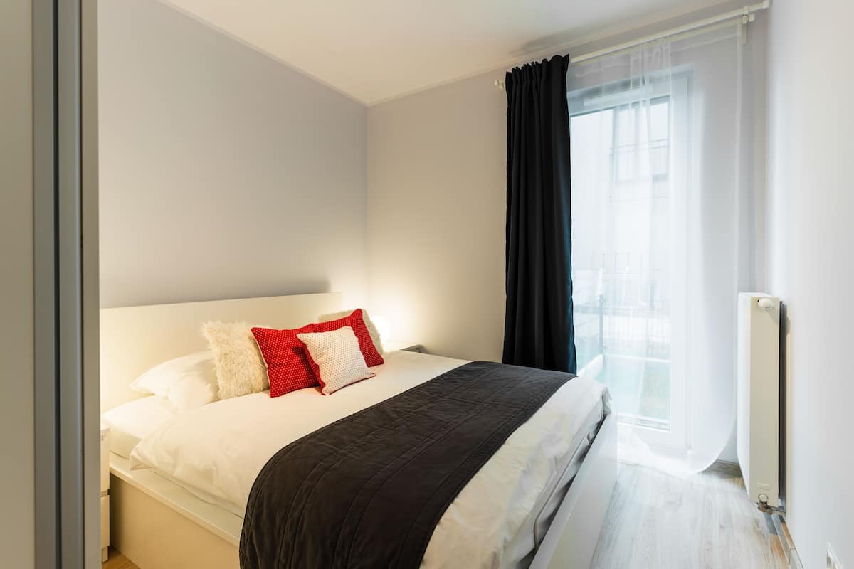 Une chambre à coucher avec un lit, des murs blancs, une fenêtre avec des rideaux et un radiateur.