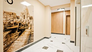 Um corredor com piso de mármore, um número '3' fixado na parede e uma porta de madeira.