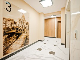 Un pasillo con suelo de mármol, un número '3' en la pared y una puerta de madera.