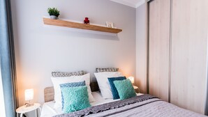 Quarto bem arrumado com cama, mesas de cabeceira, uma estante com objetos decorativos e um guarda-roupa.