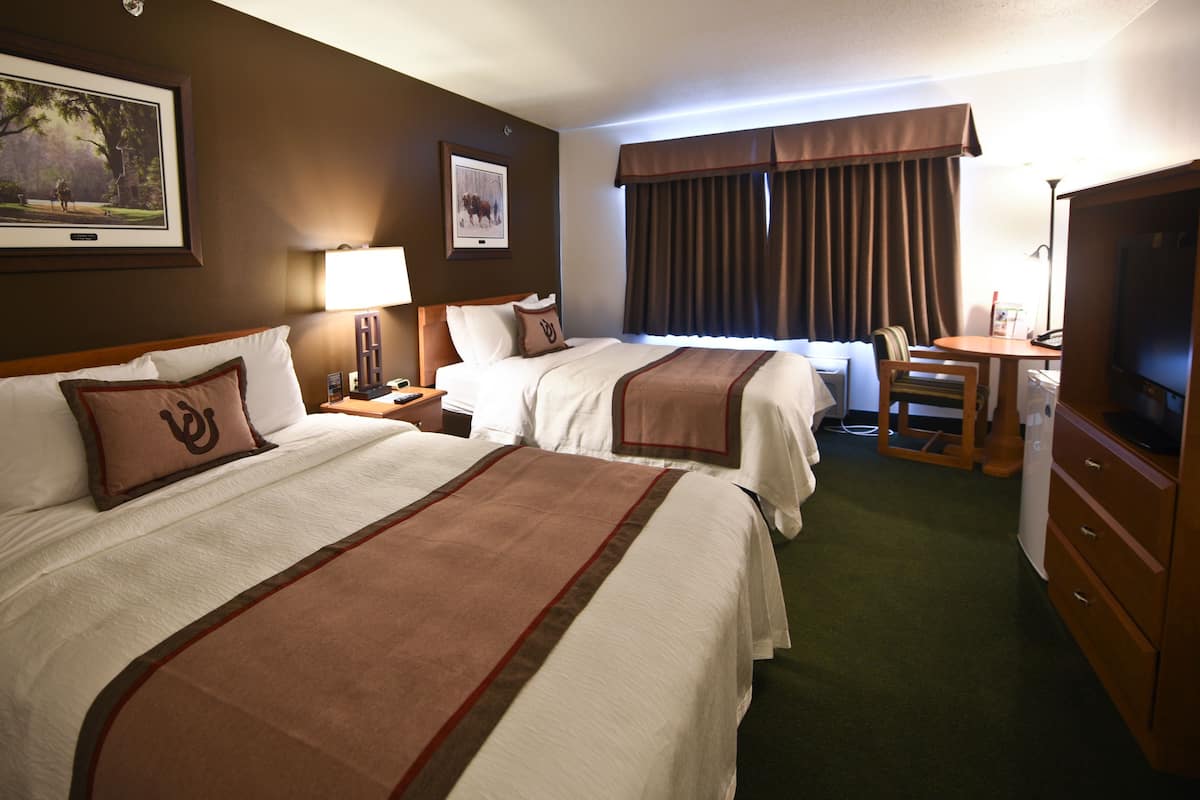 A hotel room with two beds, a desk, a television, and a window with curtains.