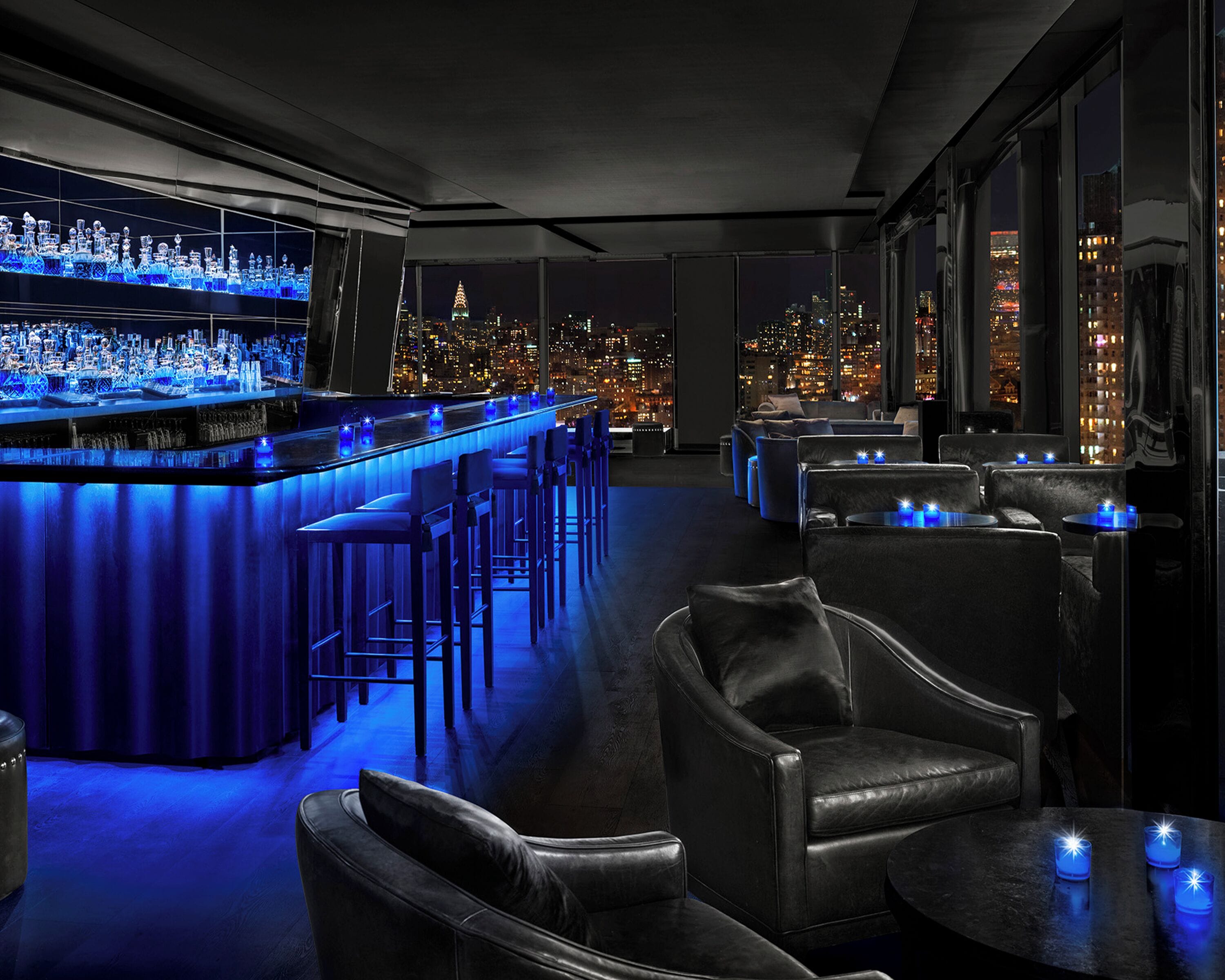 Zona do bar com vista para a cidade, assentos em couro e balcão bem iluminado.