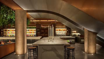 Zona de bar moderna con una isla central, taburetes y una variedad de botellas de colores en estanterías.