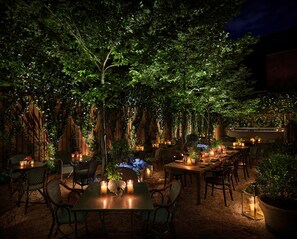 An outdoor dining area with tables and chairs, surrounded by lush greenery and wooden walls. - PUBLIC, an Ian Schrager hotel (New York)