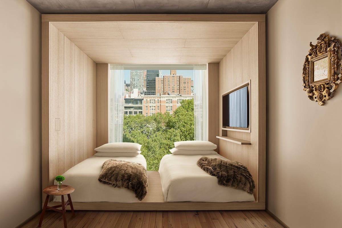 A bedroom with two beds, a TV, and a view of a cityscape through large windows.