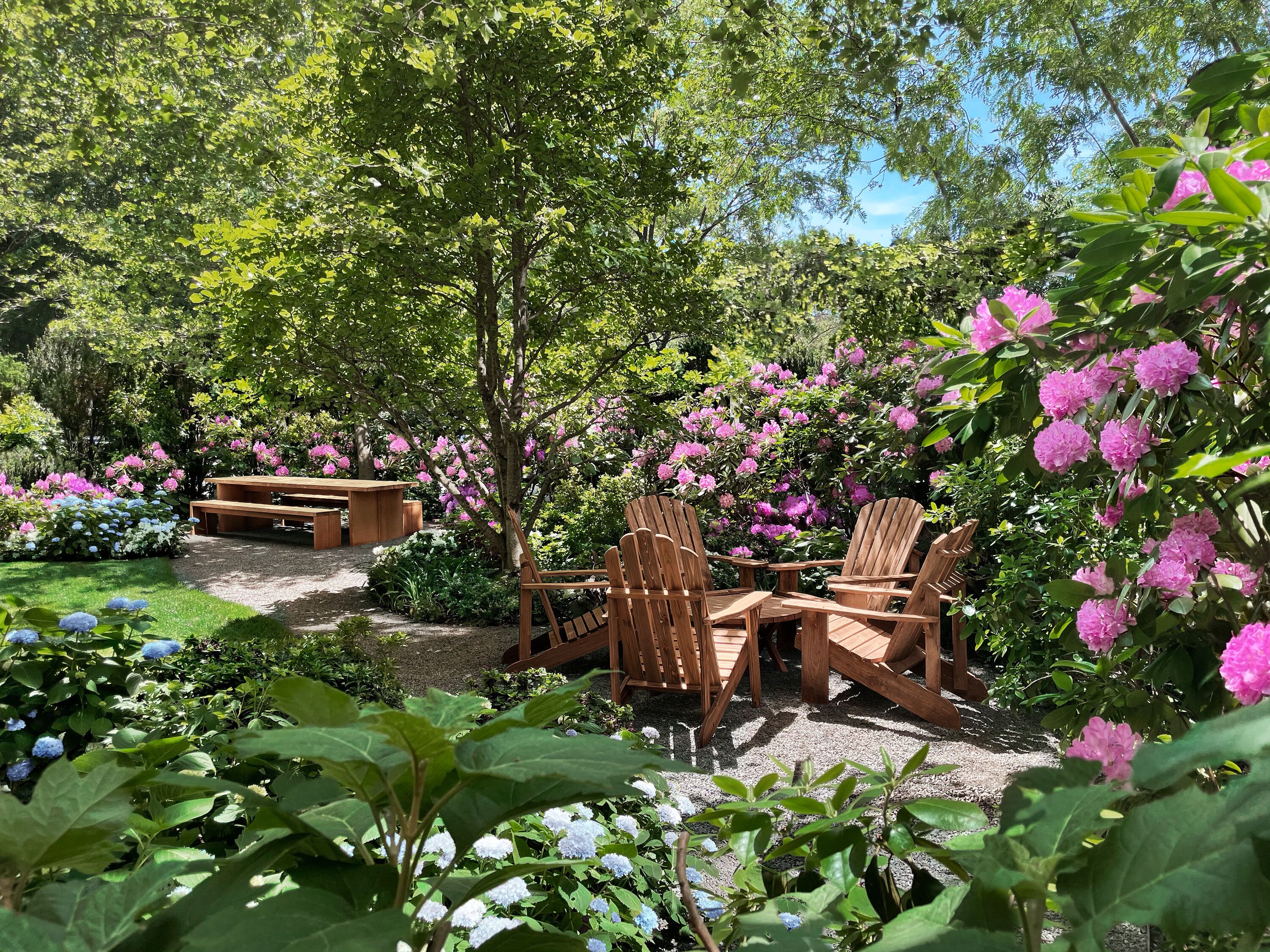 A garden with wooden furniture and blooming flowers.