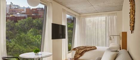 Una habitación de hotel moderna con un ventanal grande, un televisor de pantalla plana, un sofá, una mesita y una silla.
