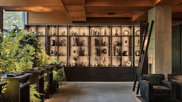 Un interior moderno con una pared decorada con diversos objetos y plantas, un suelo de hormigón y muebles de tonos oscuros.