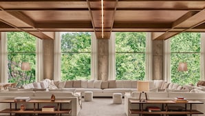 A spacious living room with a large sectional sofa, two side tables, and a view of lush greenery through large windows.