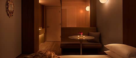 Une chambre d’hôtel avec un lit, une table ronde décorée de bougies, un plaid en fausse fourrure moelleux et un banc en bois.