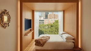 Quarto com uma grande janela, cama, televisão e piso de madeira.