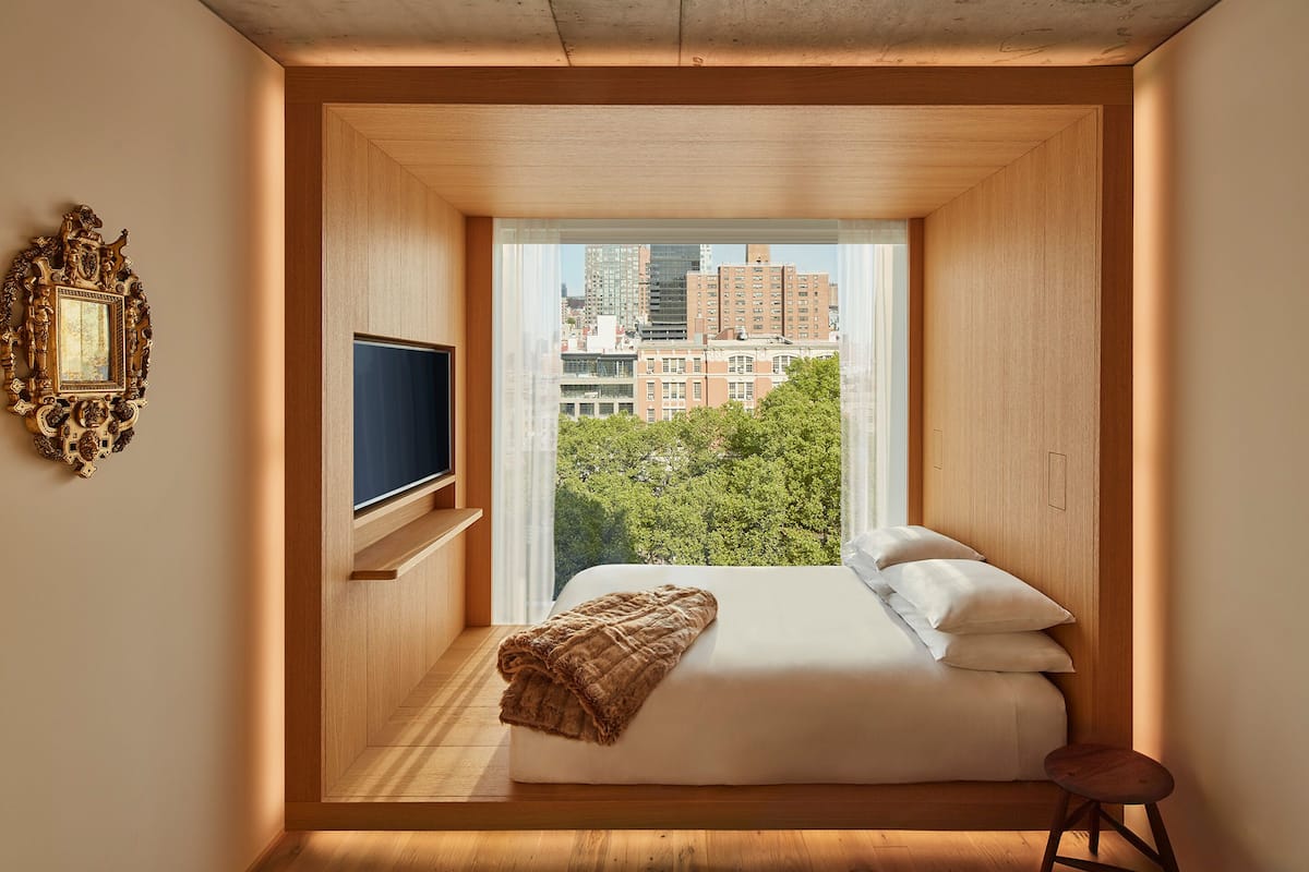 A bedroom with a large window, a bed, a TV, and a wooden floor.
