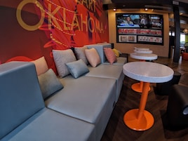 A modern lounge area with a sofa set, a round table, and a TV displaying a news program.