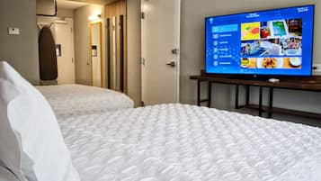 Ein Hotelzimmer mit zwei Betten, einem Fernsehgerät auf einem Standfuß und einer Tür zu einem Badezimmer.