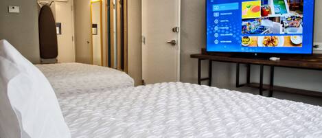 A hotel room with two beds, a television on a stand, and a door leading to a bathroom.